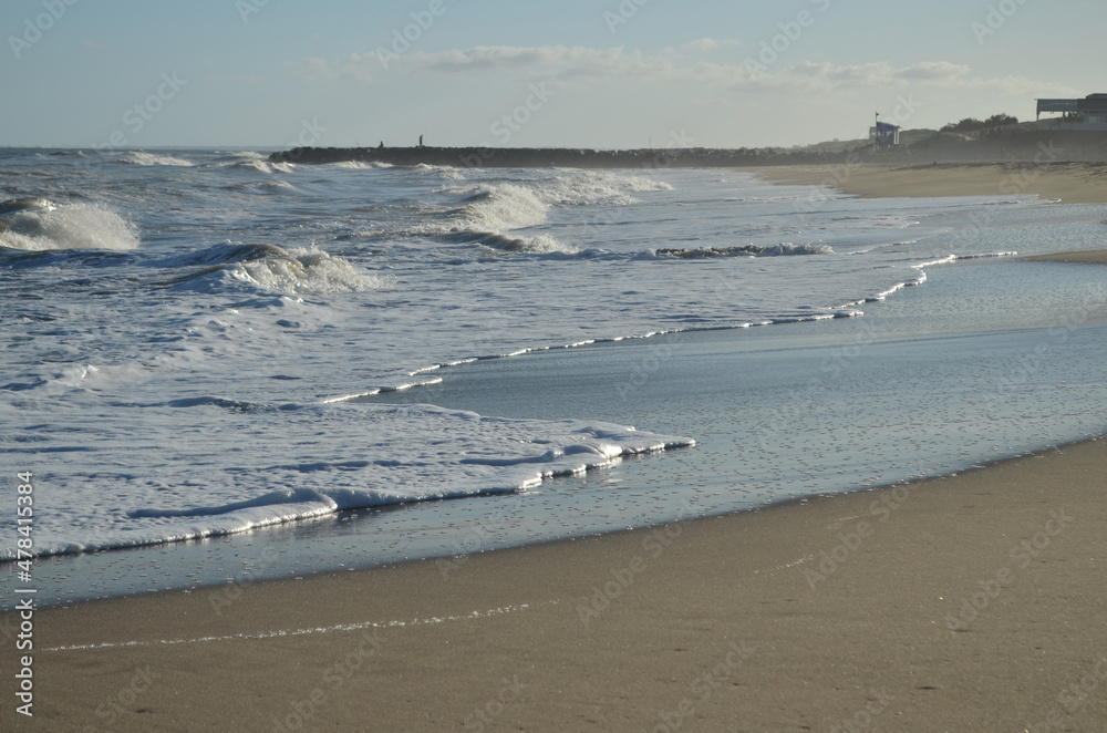 Playa, olas y a lo lejos, pescadores en el espigón