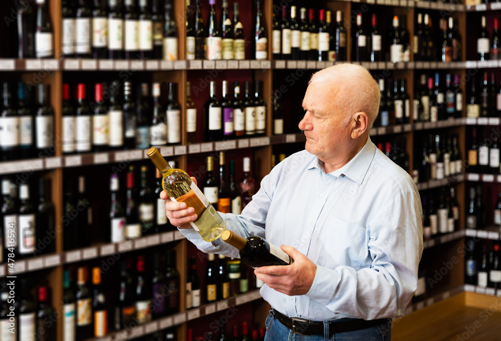 Serious mature man chooses between red and white wine in a liquor store