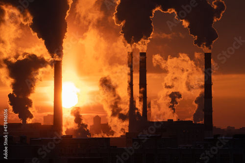 Fototapeta Chemical factory chimneys with raising smoke against red sunset sky in winter city during strong frost