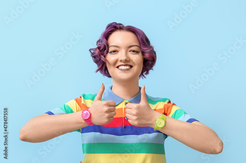 Young woman in rainbow clothes showing thumb-up on blue background. LGBT concept