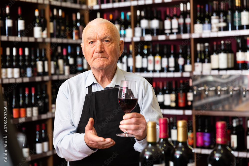 Confident elderly male winemaker inviting to wine house, offering glass of wine for tasting. High quality photo