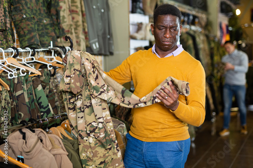 African-american man selecting outwear in military goods store.