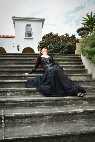  portrait of pretty female model with red hair wearing glamorous gothic black lace ballgown. Posing in a fairytale castle location with staircases 