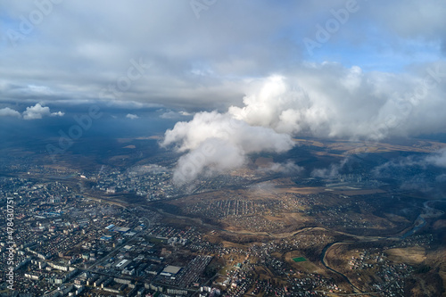 Aerial view from high altitude of distant city covered with puffy cumulus clouds flying by before rainstorm. Airplane point of view of landscape in cloudy weather © bilanol