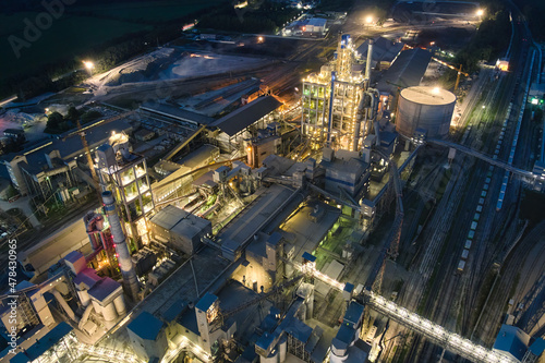 Aerial view of cement factory with high concrete plant structure and tower cranes at industrial production area at night. Manufacture and global industry concept