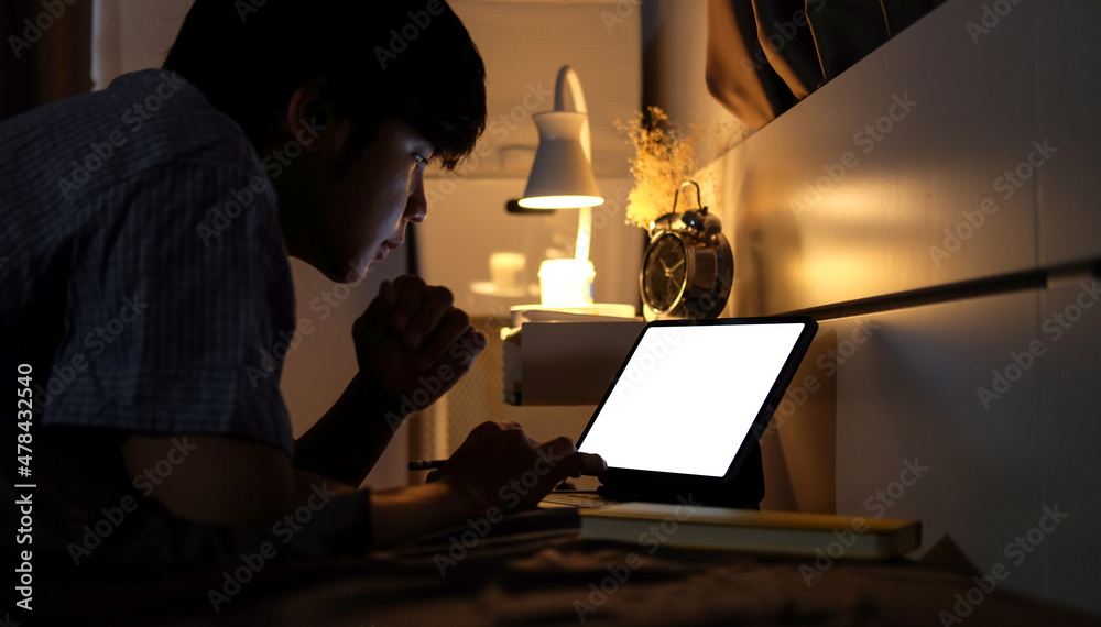 Side view young man working with computer tablet at late night on bed. Side view young man working with computer tablet at late night on bed.