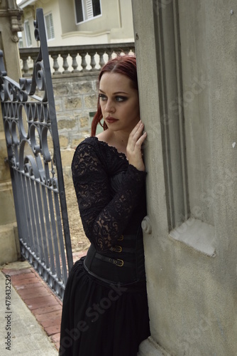  portrait of pretty  female model with red hair wearing glamorous gothic black lace ballgown.  Posing in a fairytale castle location with staircases 