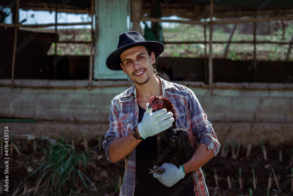 Close-up of Portrait of a cheerful farmer holding and taking care of chicken outdoor. A smart hipster young man holding a hen has been satisfied smiling at an organic sustainable egg farm