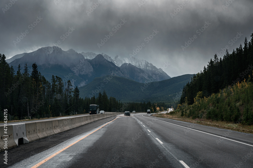 Naklejka premium Car driving on highway with rocky mountains and moody sky in overcast day at Banff national park