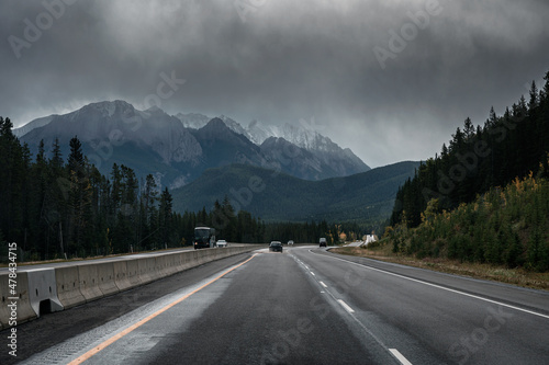 Car driving on highway with rocky mountains and moody sky in overcast day at Banff national park