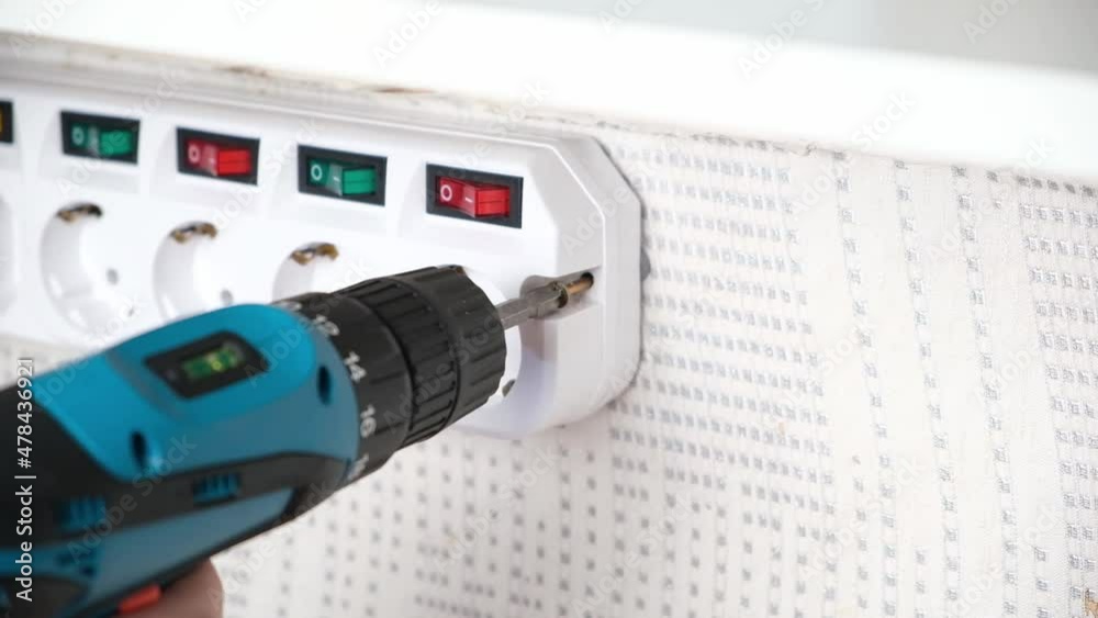 A man tightens a screw with a screwdriver to attach the socket adapter with switches to the wall. A man tightens a screw with a screwdriver to attach the socket adapter with switches to the wall.