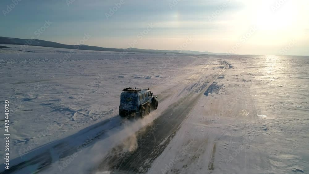 Aerial shot of an off-roader all-terrain vehicle SUV drives on snow and ice covered surface of Lake Baikal. Winter landscape. Popular tourist destination. Aerial shot of an off-roader all-terrain vehicle SUV drives on snow and ice covered surface of Lake Baikal. Winter landscape. Popular tourist destination.