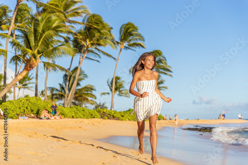 Summer vacation happy Asian woman running carefree on beach during Hawaii travel on Maui island wearing white dress at sunset.