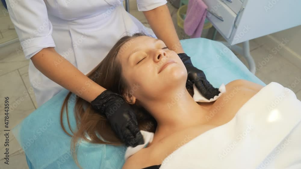 Cosmetologist wipes neck and chest of young woman from dirt with wet white sponges. She gently rubs the patient's fair skin to clean it of impurities. Cosmetology, acne treatment, acne, rejuvenation