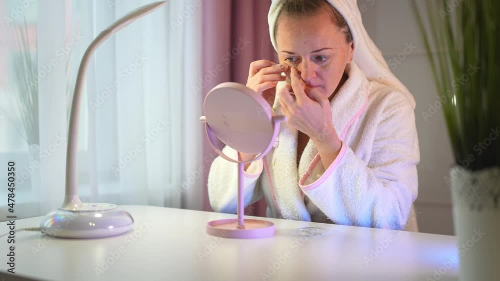 Young woman at home in front of the mirror puts patches on her eyes