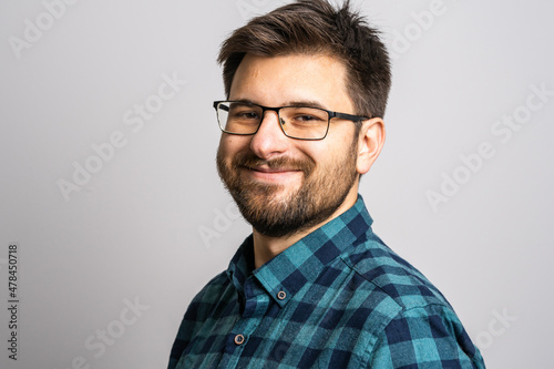 Portrait of one adult caucasian man 30 years old with beard and eyeglasses looking to the camera in front of white wall background smiling wearing casual shirt copy space © Miljan Živković