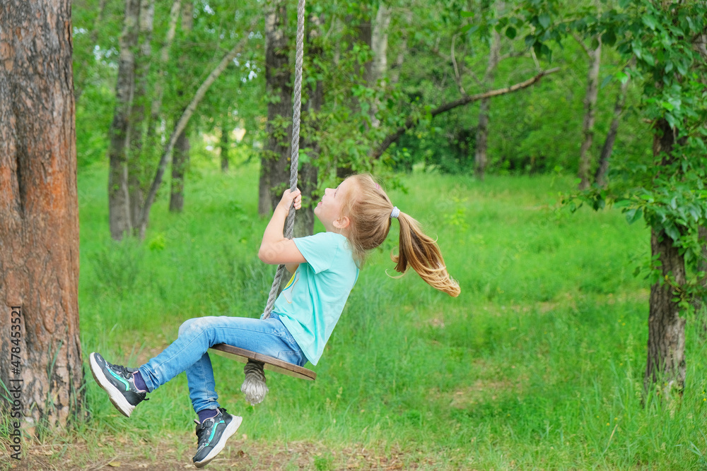 Child having  fun outdoors swinging on wooden homemade swing tied to a tree with a rope in spring or autumn.