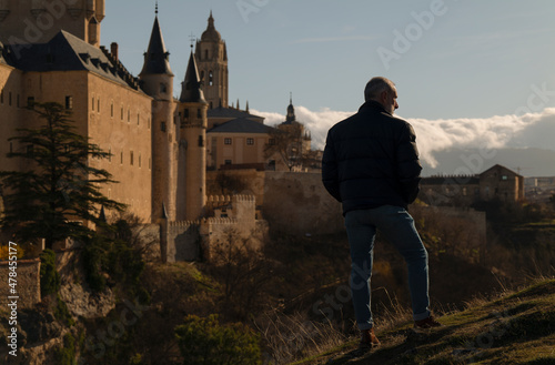 Portrait of adult man in winter clothes standing on hill looking at skyline of city. Segovia, Spain