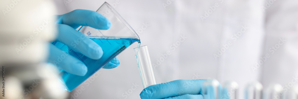Scientist with gloves pours blue liquid into test tube in laboratory