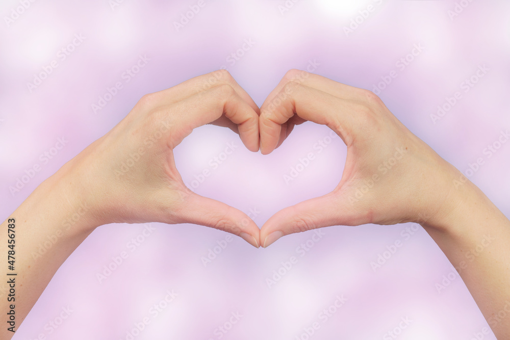 Fototapeta premium female hands in the shape of a heart on a pink bokeh background.