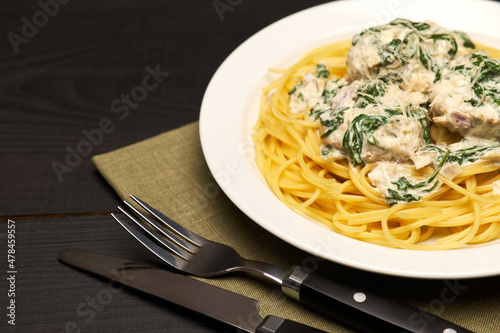 Portion of delicious meatballs with spinach in a creamy sauce and pasta on wooden background