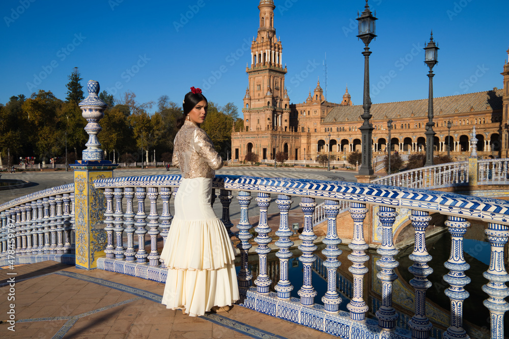 Flamenco dancer, woman, brunette and beautiful typical Spanish woman is looking at the camera leaning out of an Andalusian tiled railing. Flamenco concept of cultural heritage of mankind
