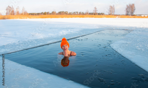 Winter swimming. The woman in the ice hole of the frozen lake. Wellness for swimmers in icy water. Beautiful woman in zen meditation.
