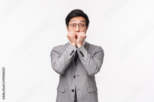 Waist-up portrait of surprised and impressed young handsome asian businessman gossiping with coworker, being amazed gasping, cover mouth and staring thrilled camera, white background