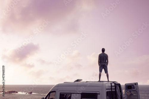 Man standing on top of a camper van next to the ocean Fototapete