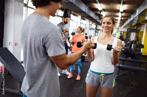 Fit happy woman with her personal fitness trainer in the gym exercising with dumbbells