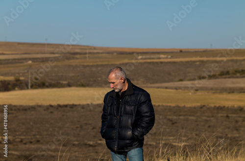 Portrait of adult man in winter clothes standing on fields against blue sky © WeeKwong