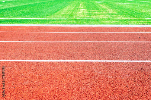 Side view of a running track in a stadium and part of a soccer field with green artificial turf. Background, copy space