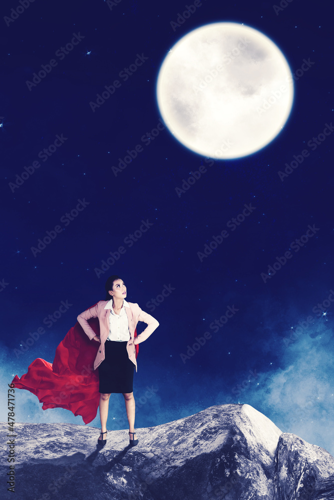 Super businesswoman looking at the moon on cliff