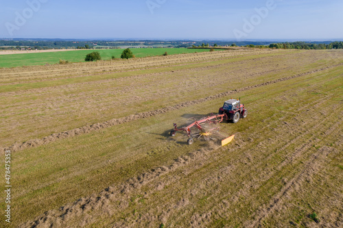 Aerial view on a tractor that collects hay in rows with a disc rake. Farmer stores fodder for cattle in summer season.