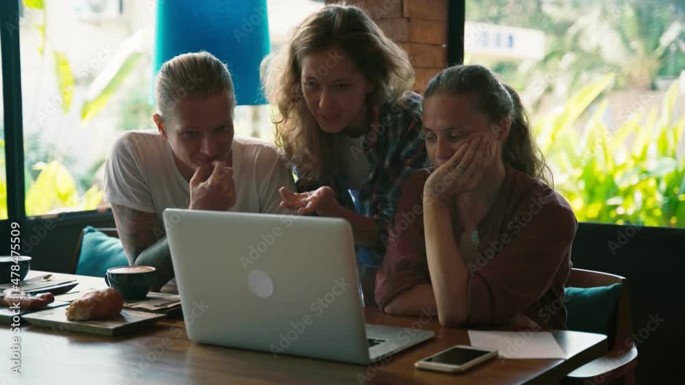Three young entrepreneurs discuss their startup project while sitting in front of a laptop in a cafe or coworking space. Concept of starting a small business with friends. Three young entrepreneurs discuss their startup project while sitting in front of a laptop in a cafe or coworking space. Concept of starting a small business with friends.