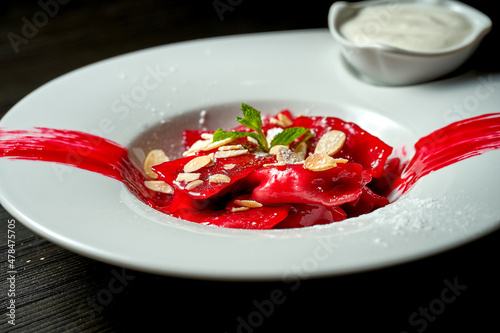 Classic Ukrainian Pierogi or Varenyky with cherries, red sauce, sour cream and almonds in a white plate.