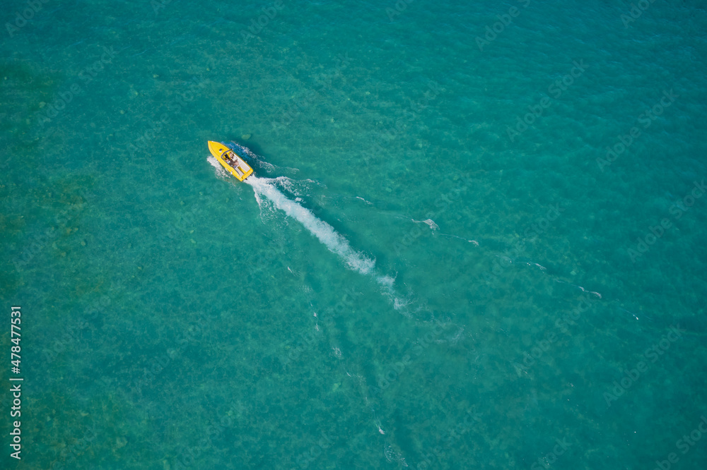 Yellow high-speed luxury boat with people moving on turquoise water. Boat performance fast movement on clear water aerial view.