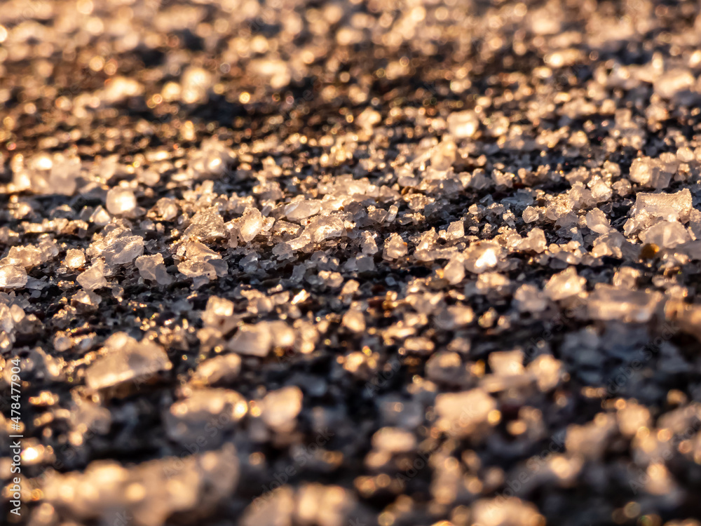 Salt grains on icy sidewalk surface in the winter. Applying salt to keep roads clear and people safe in winter weather from ice or snow. Macro view of salt grains with winter scenery in bacground Salt grains on icy sidewalk surface in the winter. Applying salt to keep roads clear and people safe in winter weather from ice or snow. Macro view of salt grains with winter scenery in bacground
