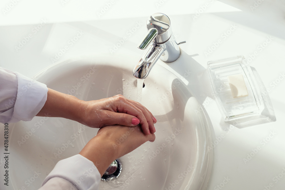 Woman washing hands rubbing with soap in white sink in bathroom with sunlight from the window. Protection from bacteria and virus. Hygienic concept. Top view Woman washing hands rubbing with soap in white sink in bathroom with sunlight from the window. Protection from bacteria and virus. Hygienic concept. Top view