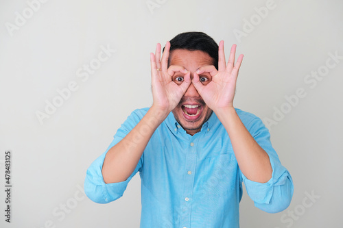 Funny Asian man peeking from his own hand and showing surprised expression photo