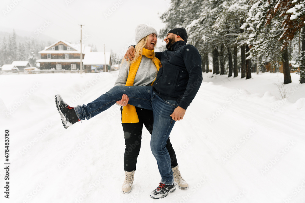 Attractive man and woman cuddling in the frosty forest. Adult couple in sweaters have fun on walk. Romantic date in winter time.Winter lovestory
