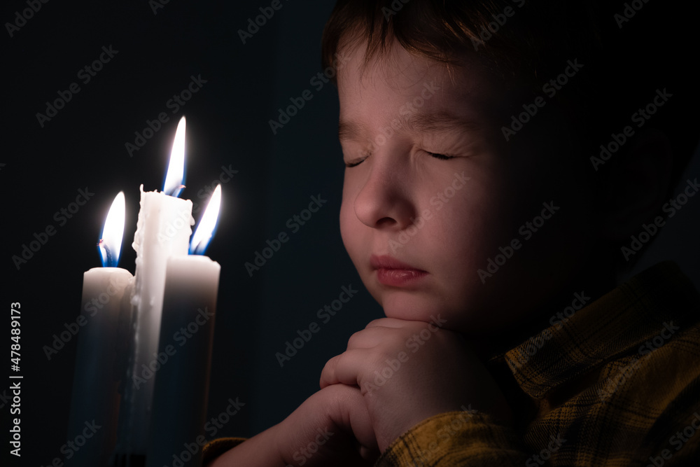 Little cute boy praying in front of a burning candle