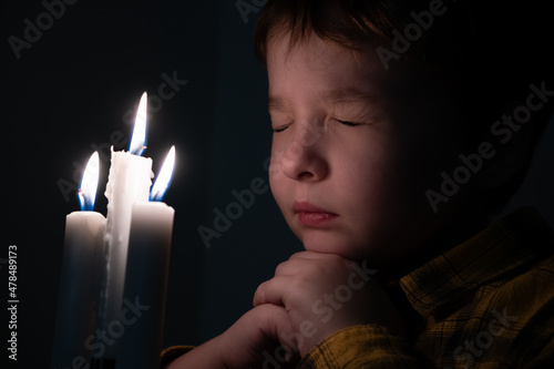 Obraz na płótnie Little cute boy praying in front of a burning candle w salonie