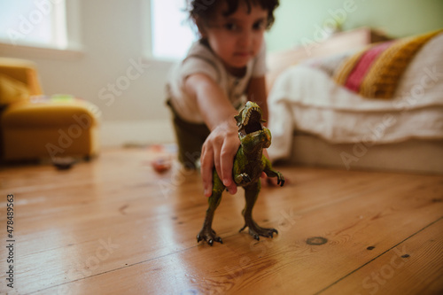 Ethnic boy playing with a t-rex dinosaur at home