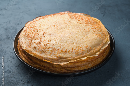 A stack of traditional fried thin pancakes on a dark gray-blue background. Maslenitsa, Russian blini. Top view.