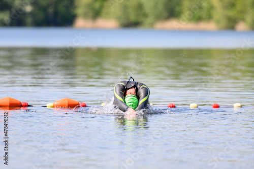 Swimmer diving into the water outdoor in nature with a green swimming cap while wearing a wetsuit