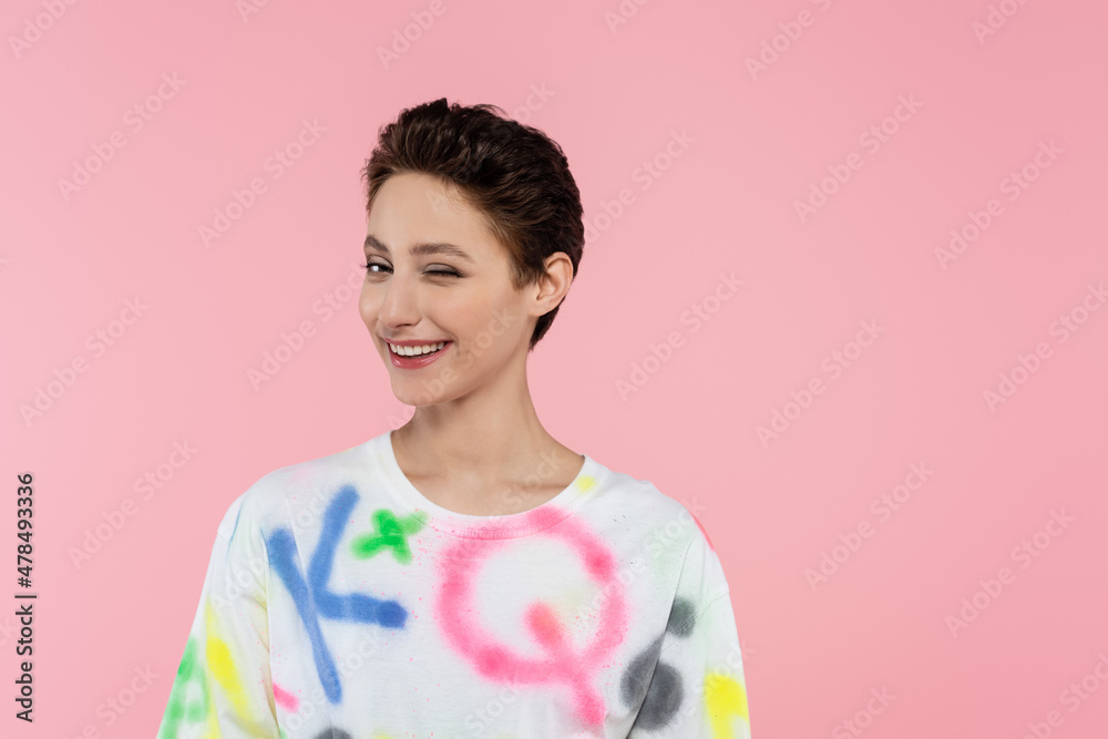 cheerful brunette woman in trendy t-shirt winking at camera isolated on pink cheerful brunette woman in trendy t-shirt winking at camera isolated on pink