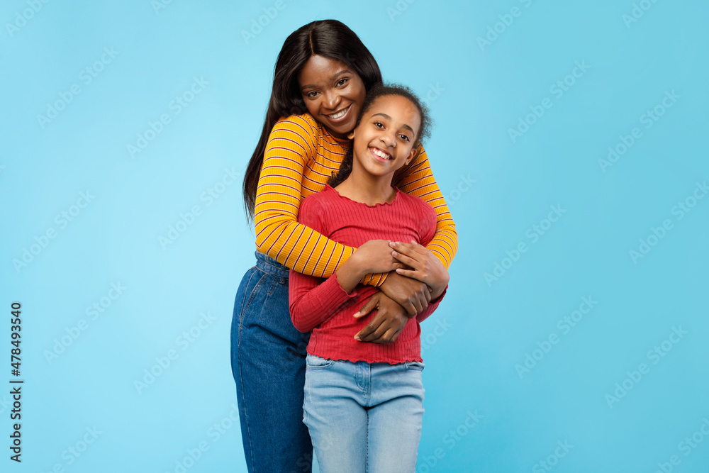 African American lady hugging her smiling daughter from the back African American lady hugging her smiling daughter from the back
