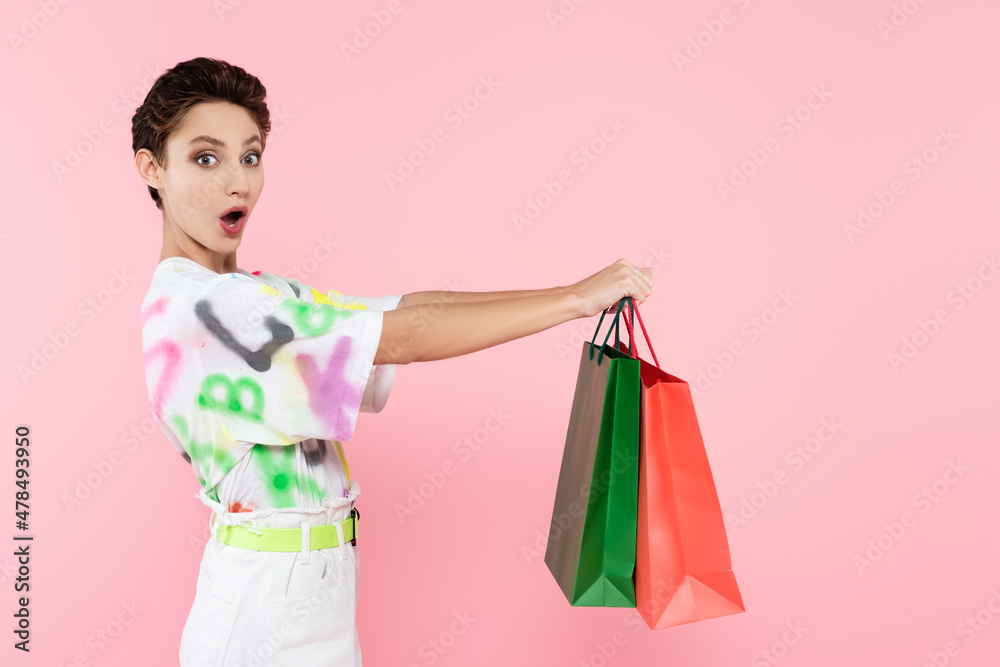 astonished woman with open mouth holding shopping bags and looking at camera isolated on pink astonished woman with open mouth holding shopping bags and looking at camera isolated on pink