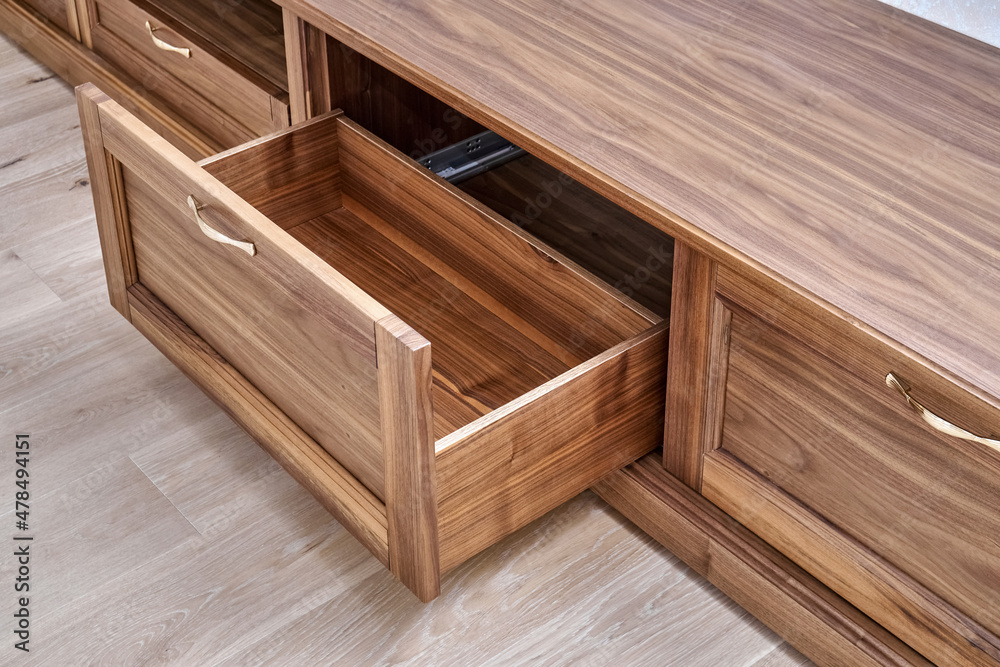 Elegant new TV cabinet made of veneer and solid walnut lumber with gold handles near wall in light room close upper view